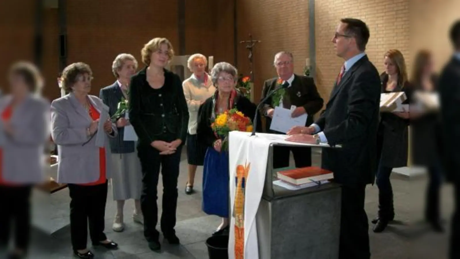 Caritas-Leiter Ulrich Prasser (am Ambo) war in die Pfarrei St. Markus gekommen, um Ehrungen an langjährige Sammler/innen zu überreichen. Dabei hob er ganz besonders Pfarreimitglied Emmy Kraft (mit Blumenstrauß) hervor, die sich in vielen Bereichen engagiert. (Foto: Alfred Lehmann)
