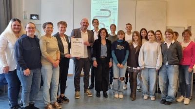 Die Schulfamilie freut sich über die von Ministerialbeauftragten Sonja Kalisch (4. von links) überreichte Urkunde. Im Bild von links: drei Vertreterinnen des Elternbeirats, Sonja Kalisch, Schulleiter Harald Kraus, die Lehrkräfte Sebastian Geisler und Jelena Tuba , die die Projettag mit organisiert haben, zusammen mit besonders engagierten Schülerinnen. (Foto: Schule / Isabel Voigt)