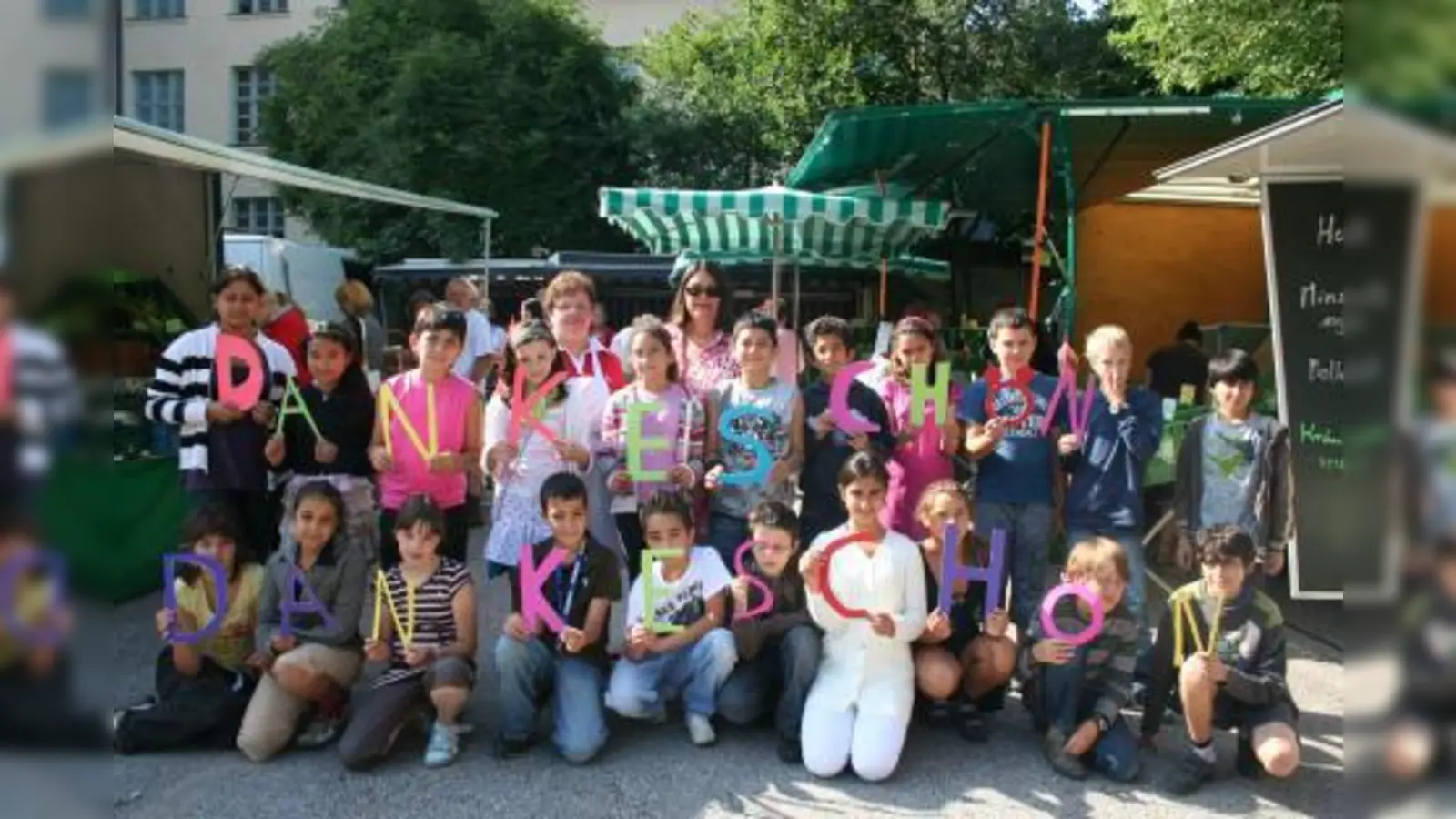 Die Klasse 4 c der Grundschule an der Fürstenrieder Straße formte aus bunten Buchstaben ihr „Danke schön” für eine Spende der Händler des Laimer Bauernmarktes. Im Bild (v.l.): Angela Christof, Markt-Sprecherin und Christine von Sprenger, Rektorin. (Foto: tg)