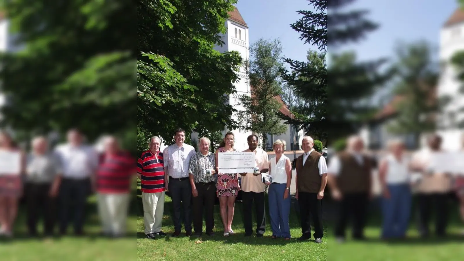 Im Hintergrund die wunderschöne Aubinger Pfarrkirche St. Quirin, für deren Renovierung jetzt die Scheckübergabe stattfand: (von links) die beiden Bäckermeister Richard Mayer senior und junior, Kirchenpfleger Gerhard Fleck, Julia Mayer, Ehefrau des Juniorchefs, Pater Georg sowie Gisela Busch und Anton Fürst von der Projektgruppe „Kirchenrenovierung St. Quirin“. (Foto: Eva Schraft)
