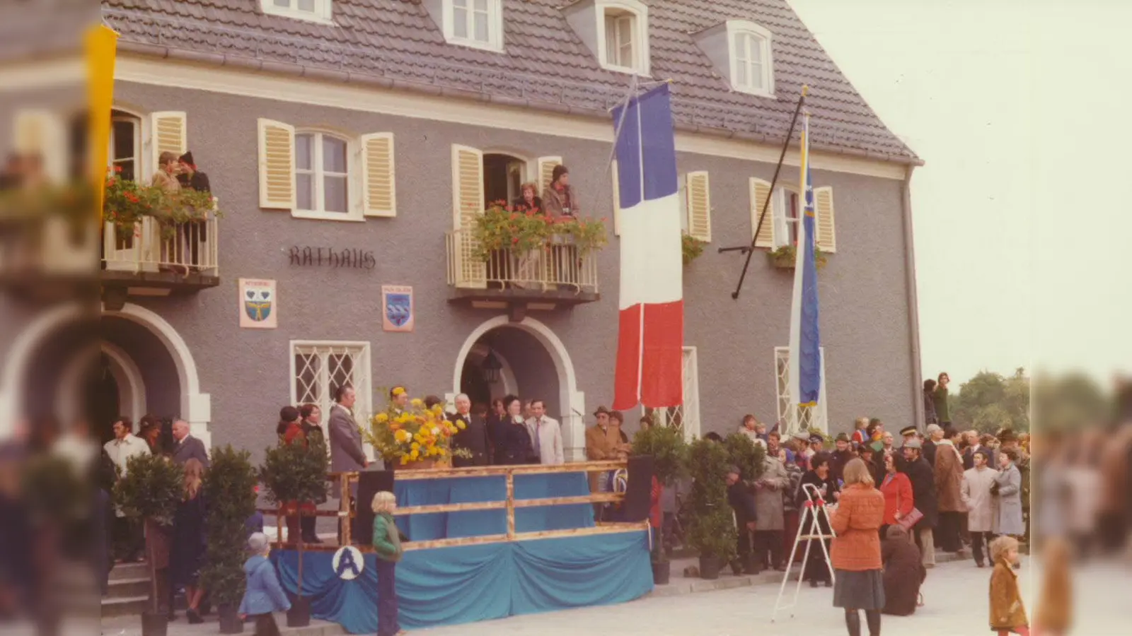 Das Neubiberger Rathaus im Flaggenschmuck nach der Enthüllung der Wappentafeln mit Festgästen und Zuschauern aus der französischen Partnerstadt im Oktober 1975. (Foto: Gemeindearchiv Neubiberg)