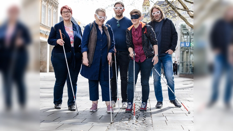 Stefanie Freitag (BBSB), Sofia Langmeier (Die Grünen), Stefan Jagl (Die Linke), Barbara Likus (SPD) und Roland Hefter (SPD) testen in der Fußgängerzone – ausgestattet mit Langstöcken und Simulationsbrillen – den sogenannten Leitstreifen, eine Regenrinne aus aus Pflastersteinen. (F.: Kerstin Keysers)