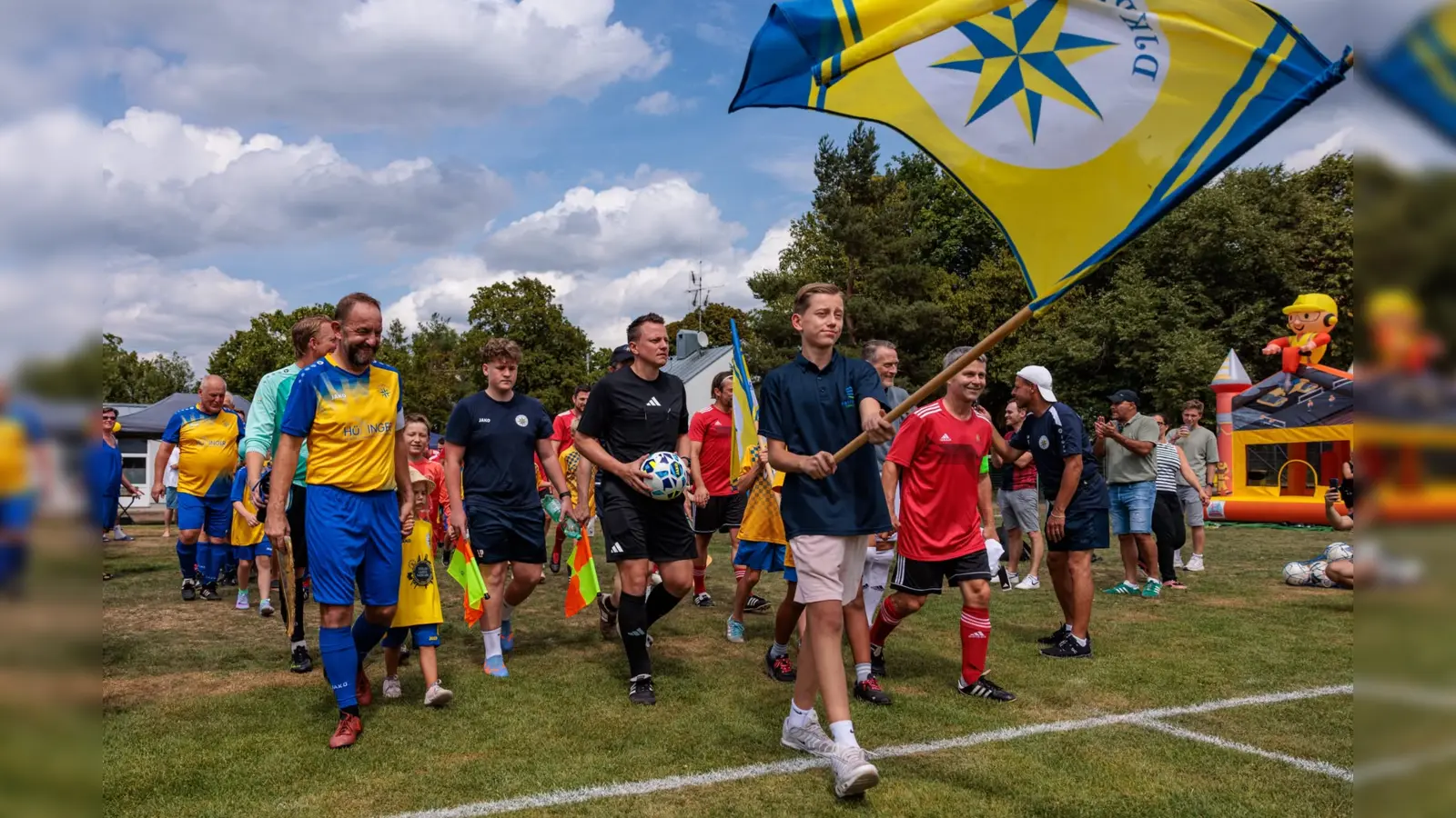 Mit wehender Vereinsfahne auf den Platz: Die DJK Pasing Allstars und der FC Sternstunden beim gemeinsamen Einlauf zum Benefizspiel anlässlich des 70-jährigen Jubiläums der DJK Pasing. (Foto: Christian Riedel/fotografie-riedel.net)