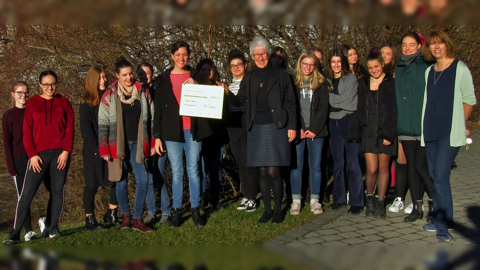 Spendenübergabe der Schülerinnen des Edith-Stein-Gymnasiums an KlinikClownin „Dr. Fiderallala“ (links vom Spendenscheck) mit Schulleiterin Hildegund Nicklas (rechts vom Scheck) und Lehrerin Nikola Trudzinski-Wagner (rechts am Bildrand). (Foto: privat)