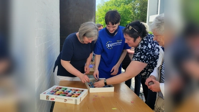 Pfarrgemeinderatsvorsitzende Dr. Andrea Hermann (1. v. l.) und Bücherei-Ehrenamtlicher Jakob Sunderer (2. v l.) legen die ersten Puzzleteile und eröffnen damit die neue Puzzle-Aktion in der Bücherei St. Martin in Germering. (Foto: St. Martin)