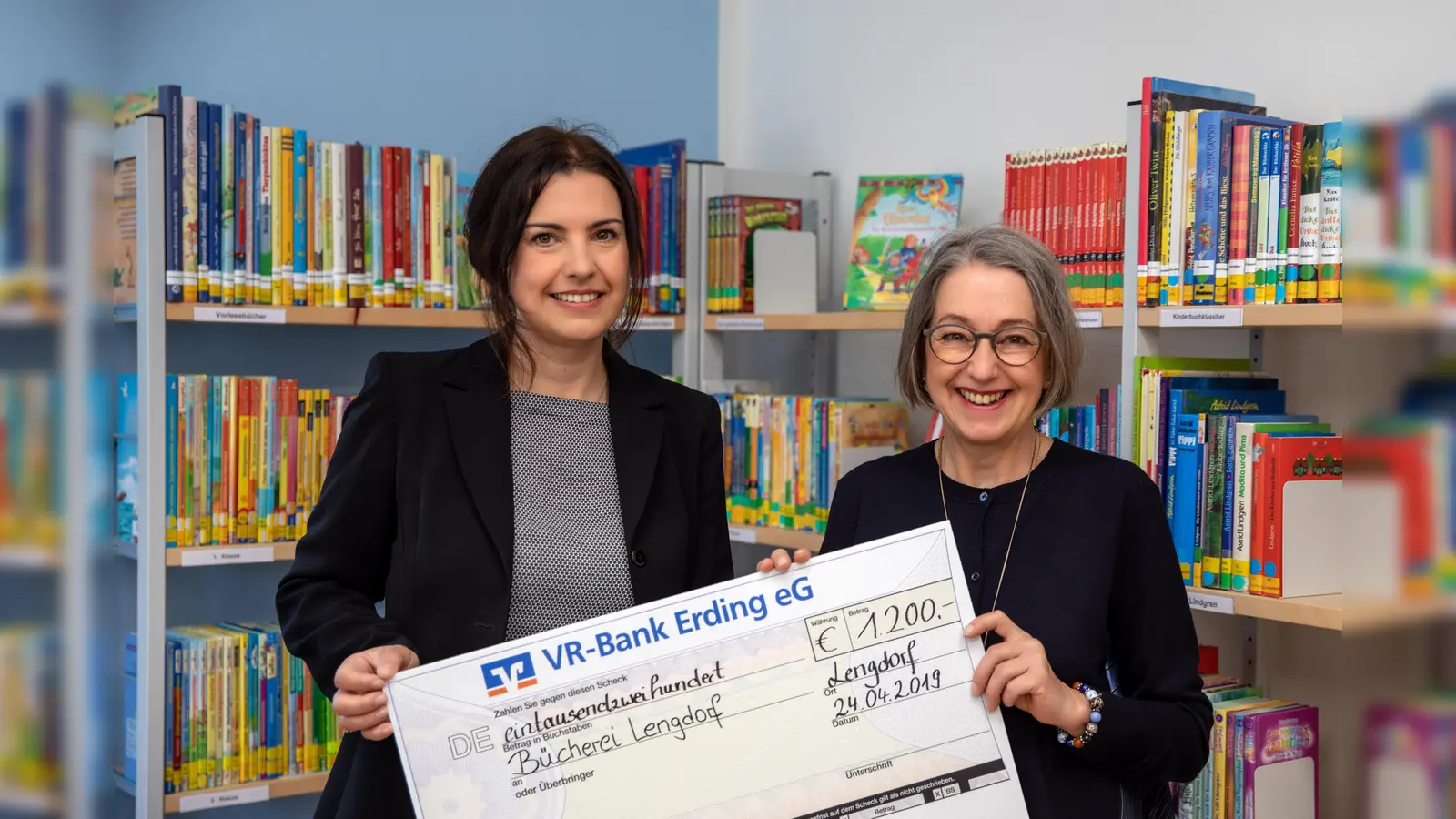 Über den Spendenscheck, den Rubina Knopf (Bereichsleitung Marktunterstützung) für die VR-Bank Erding überreichte, freute sich Rita Langheinrich (re.) stellvertretend für das gesamte Bücherei-Team. (Foto: Claus Langheinrich)