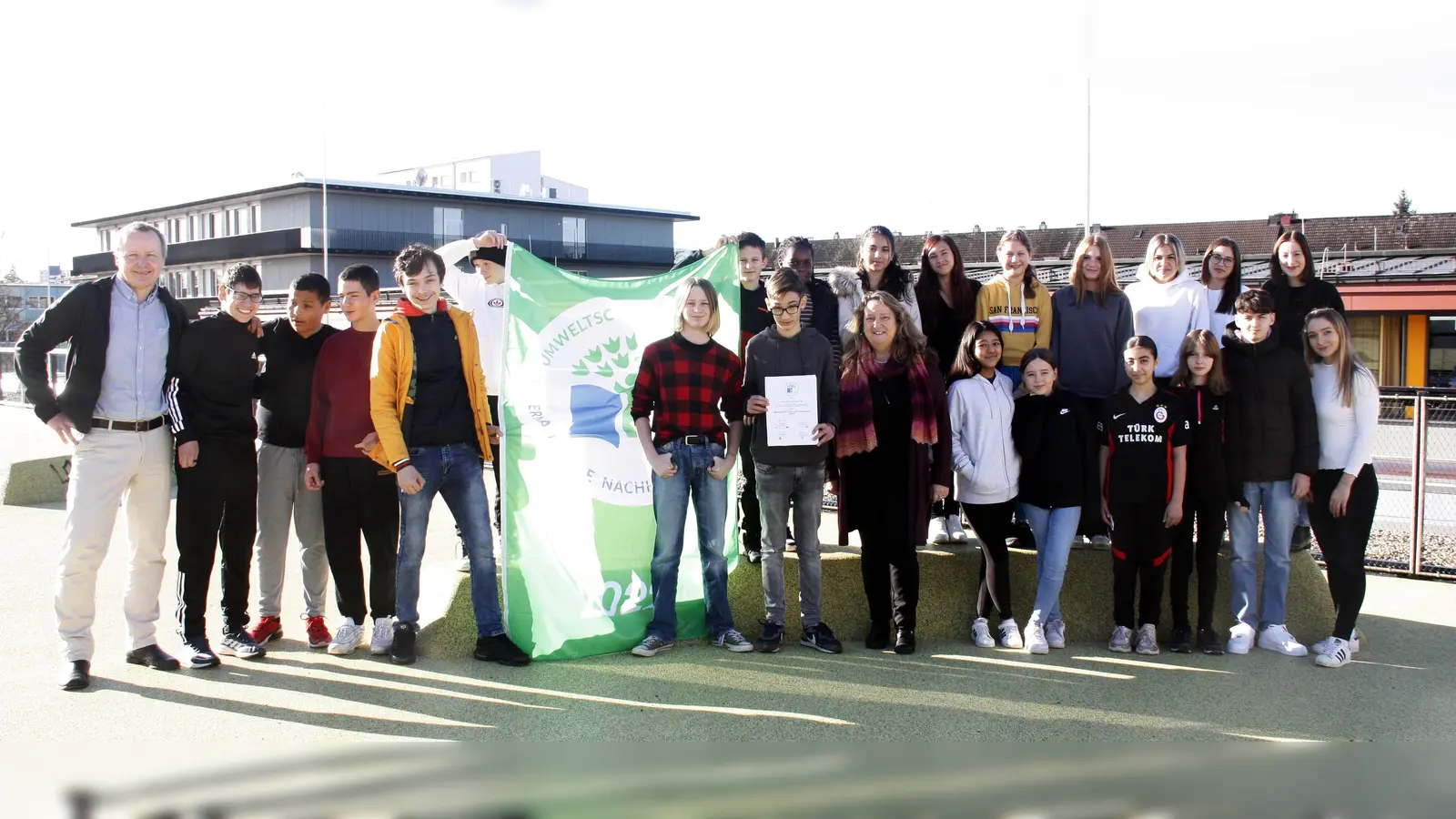 Die „Schrobis” freuen sich mit Rektor Ulrich Dendorfer (links) und ihren Lehrerinnen Johanna Bühl und Therese Moritz (rechts) auf dem Dach ihrer Turnhalle über die Auszeichnung. Stadträtin Alexandra Gaßmann (Mitte) übergab Urkunden und Fahne an die Schüler. (Foto: job)