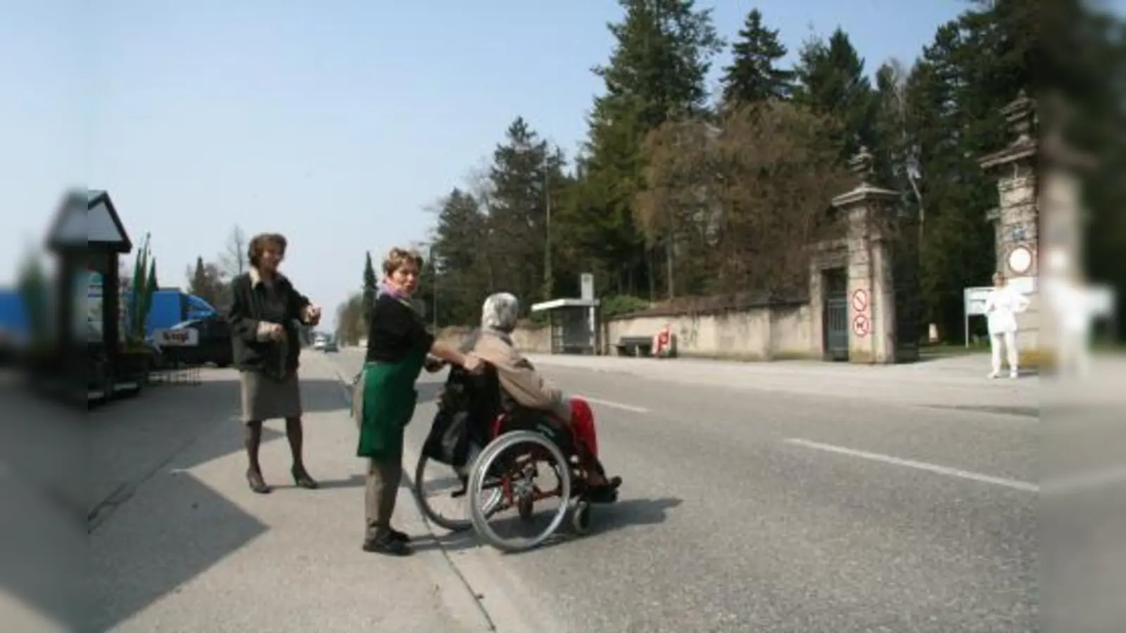 Ein sicherer Überweg über die befahrene Bergsonstraße kann noch dauern. Zwar hat das KVR den Zebrastreifen für „gleich nach den Osterferien“ versprochen, doch muss nun erst einmal ein gemeinsamer Ortstermin von VR, Baureferat und Straßenbeleuchtung gefunden werden. Auf die hilfsbereiten Helfer der Gärtnerei müssen die Querungswilligen also noch eine Weile zurückgreifen. V.l. Franziska Miroschnikoff, Gärtnerei-Mitarbeiterin Rita Straßl mit Kundin. (Foto: US)