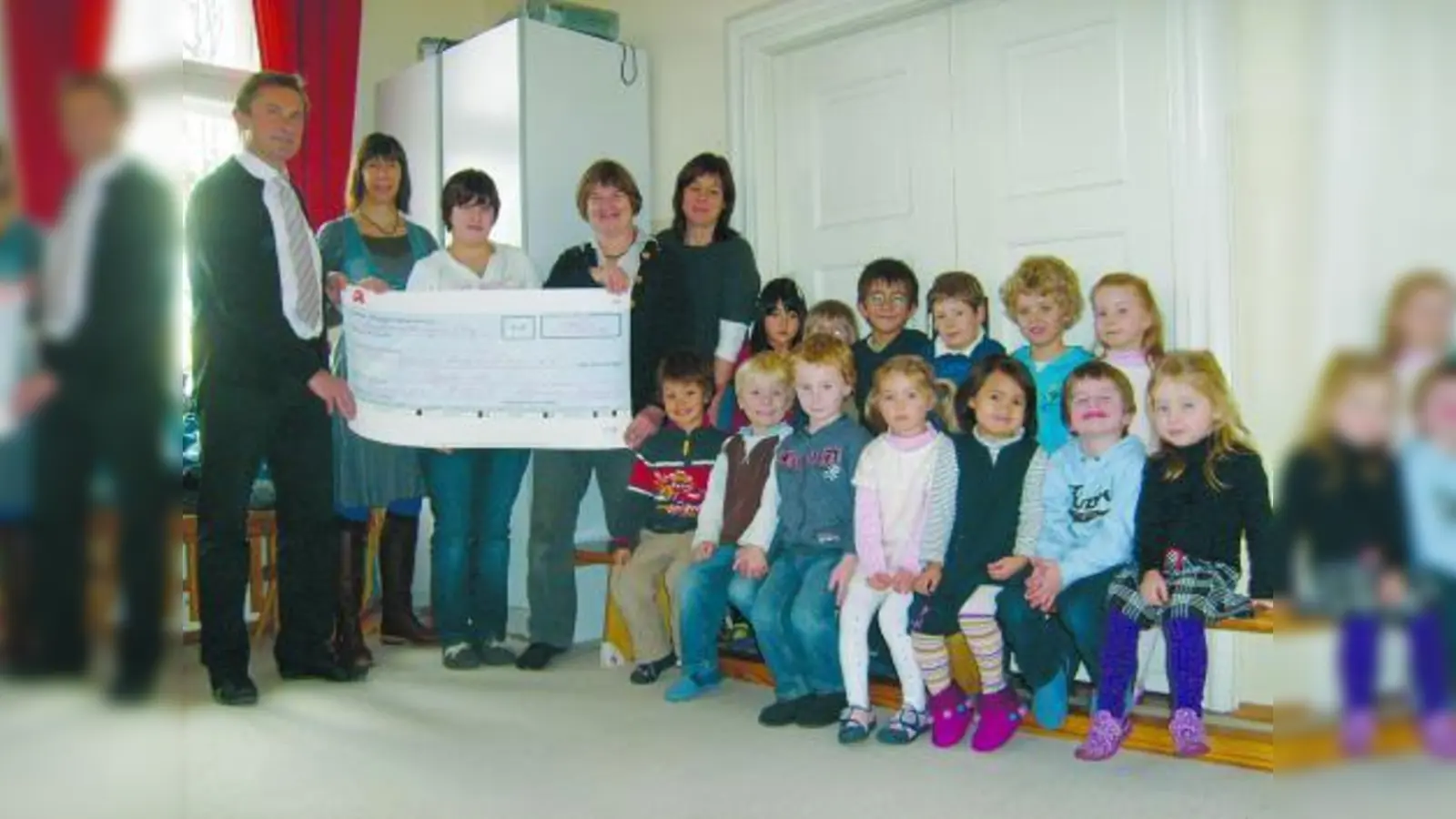 Apotheker Alfred Böhm und seine Mitarbeiterin Angelika Bergel übergeben Hannah Hofmann, Leiterin Barbara Ratering-Sommer und Andrea Finsterlin vom Montessori-Kinderhaus München-West einen Scheck über 150 Euro. Die Kleinen freuen sich mit. (Foto: pi)