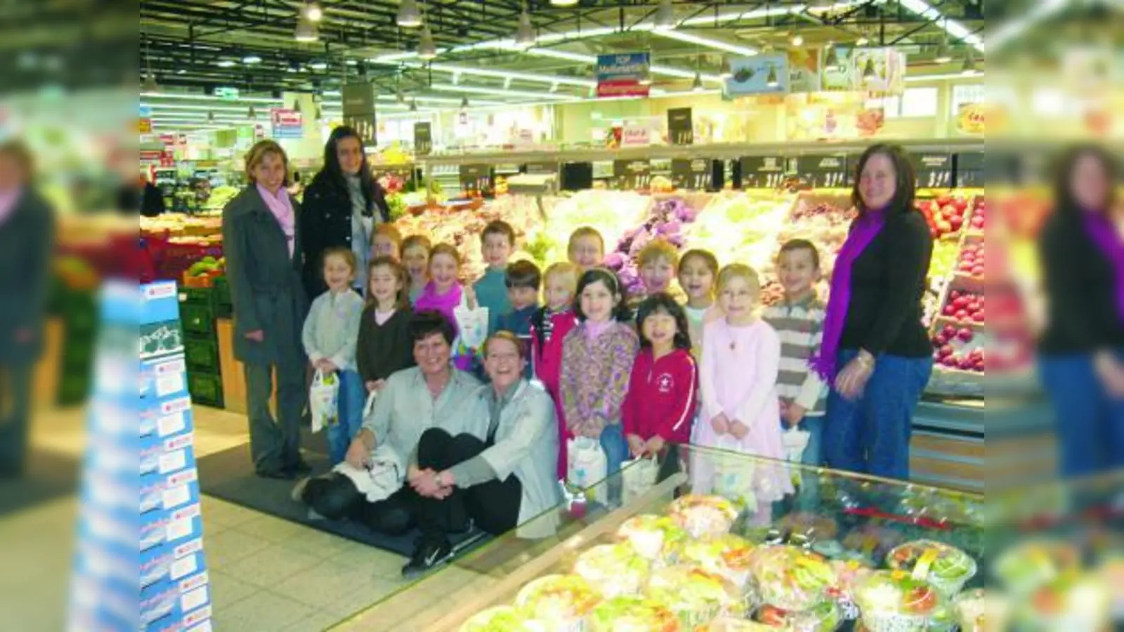 Gerhardine Maurus und Tanja Mayer (vorne) vom HIT-Markt Laim überreichten den Kindern vom Kindergarten Heilige 12 Apostel - hier mit ihren Betreuerinnen - prall gefüllte „Fruchttüten” mit frischem Obst. (Foto: pi)