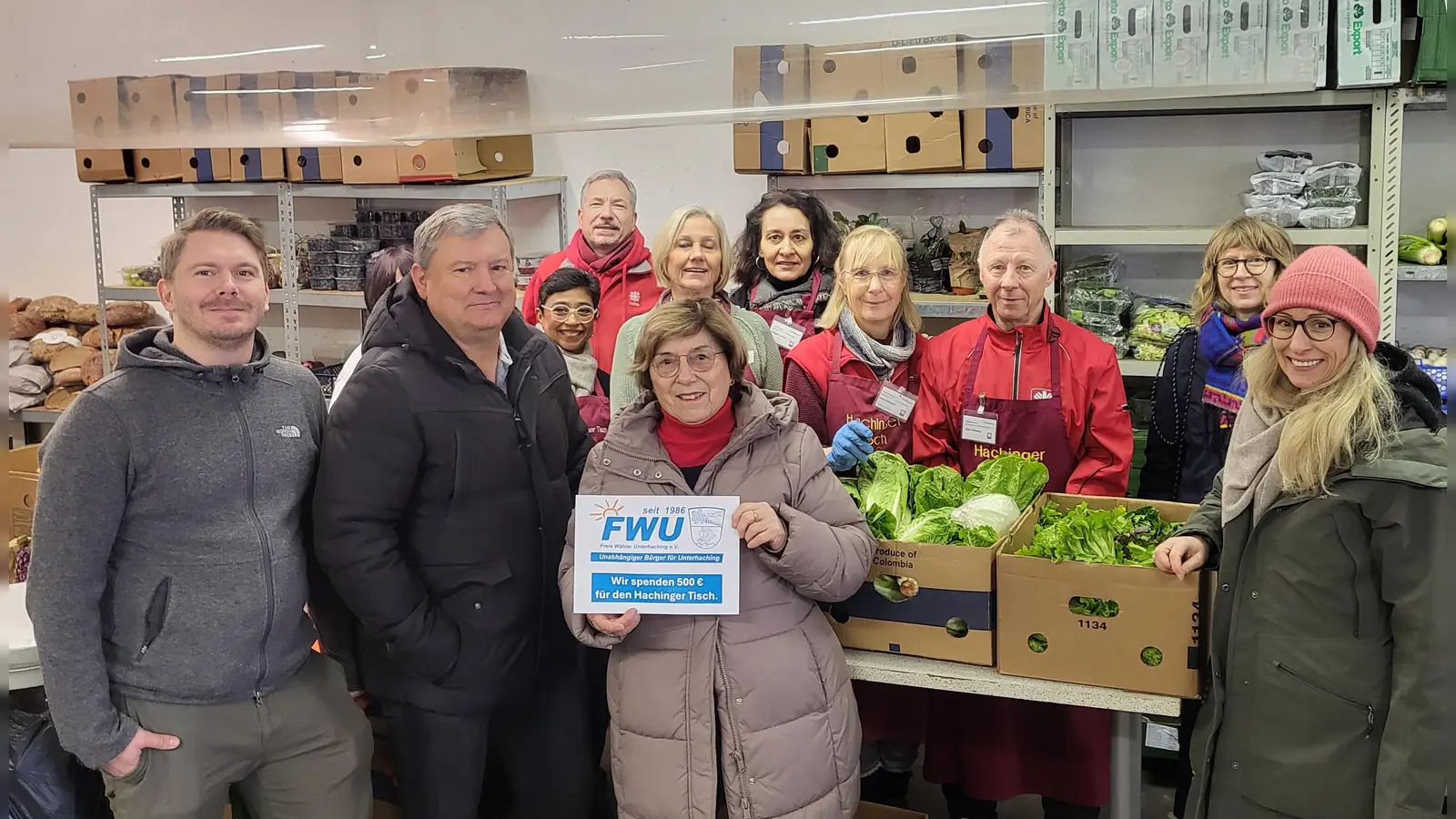 Bei der Spendenübergabe: Sebastian Ruppert, daneben: Dr. Alfons Hofstetter, in der Mitte: Dr. Christine Helming, rechts: Emily Widmann, Koordinatorin der Lebensmittelausgabe „Caritas Hachinger Tisch+”, im Hintergrund: ehrenamtliche Mitarbeiter des Hachinger Tisches. (Foto: FWU Unterhaching)