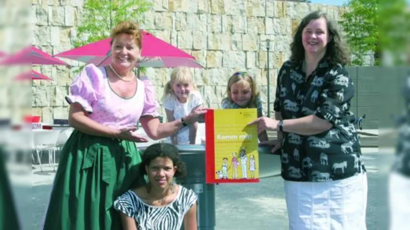 Gabriele Weishäupl (l.) und Jana Frädrich präsentieren zusammen mit Kindern die neue Broschüre „Komm-mit!”. (Foto: pi)
